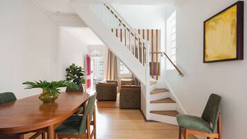 A dining area with a wooden table, green upholstered chairs, and a staircase with wooden steps and a white railing.