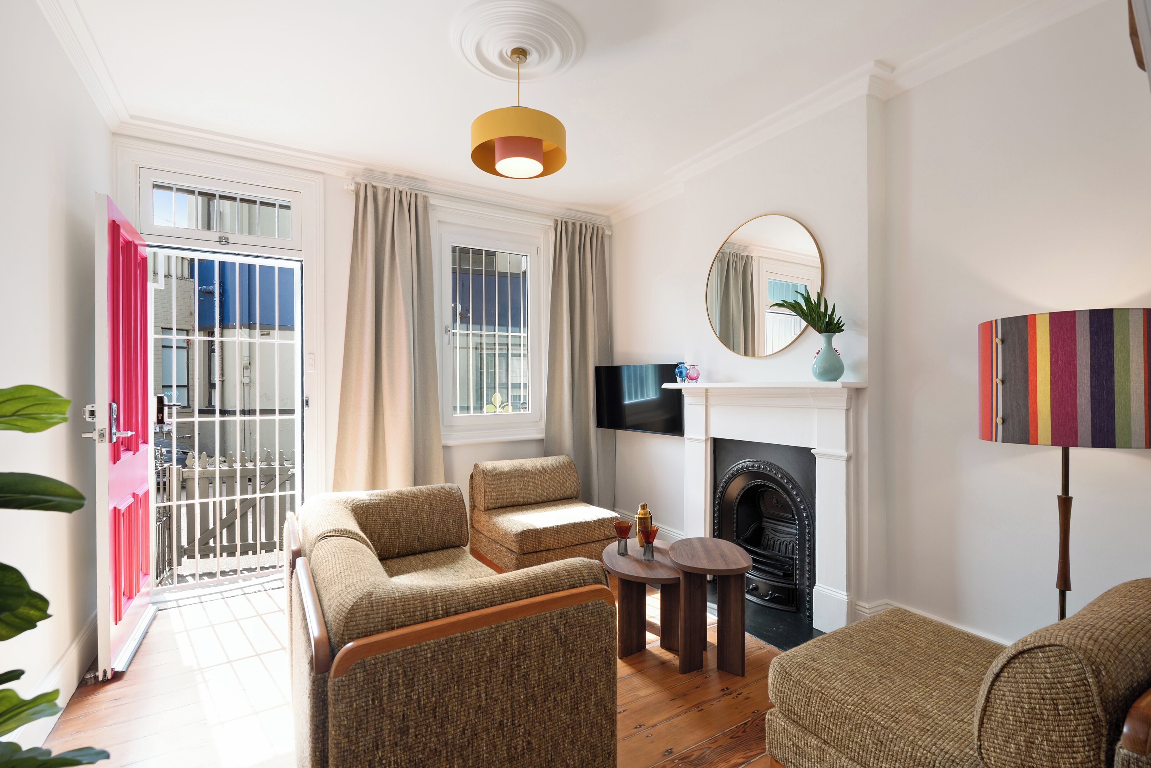 A living room with a fireplace, a round mirror, and a striped lamp.