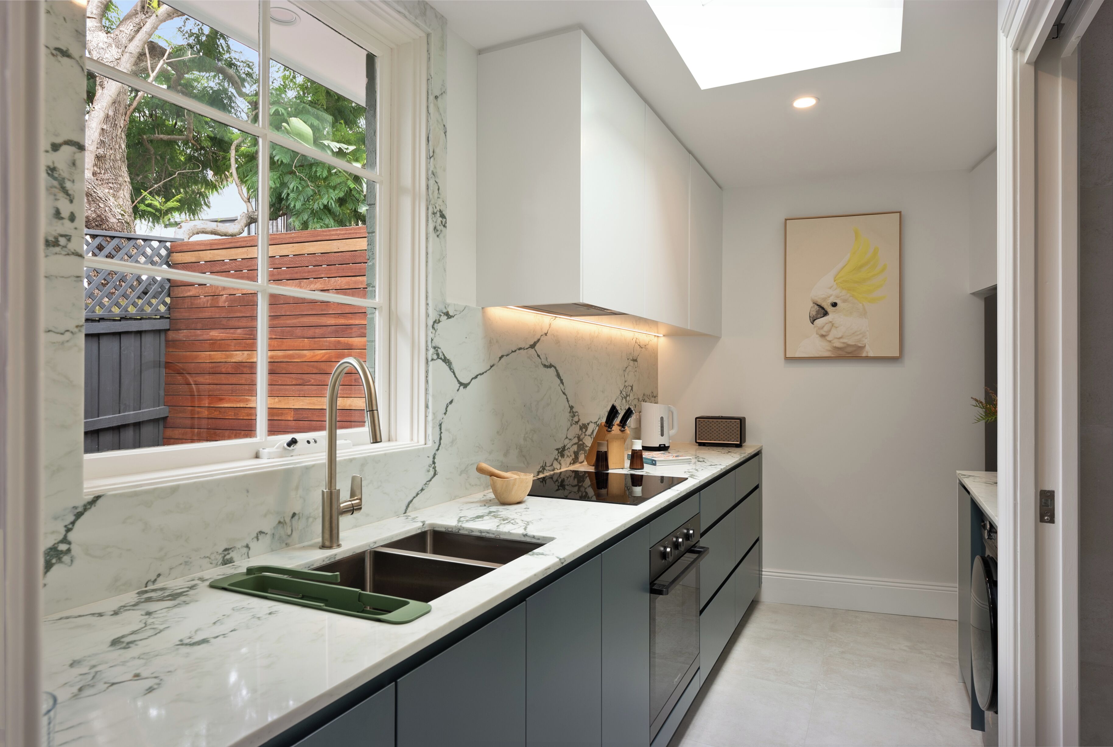 A modern kitchen with a marble countertop, a built-in oven, and a window overlooking a wooden deck.