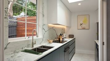 A modern kitchen with a marble countertop, a built-in oven, and a window overlooking a wooden deck.