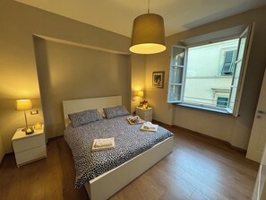 Ein Schlafzimmer mit einem Bett, Nachttischlampen, einem Fenster mit Rollläden und einer Hängelampe.