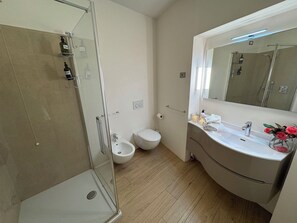 Ein Badezimmer mit einer Duschkabine, einer Toilette, einem Bidet und einem Waschtisch mit Spiegel.