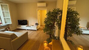 Ein Wohnzimmer mit einer Couch, einem Fernseher, einem weißen Schrank, einem großen Spiegel und einer Zimmerpflanze.
