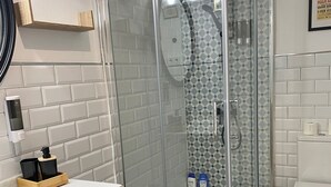 Un baño moderno con ducha de vidrio, inodoro blanco y lavamanos con dispensador de jabón.