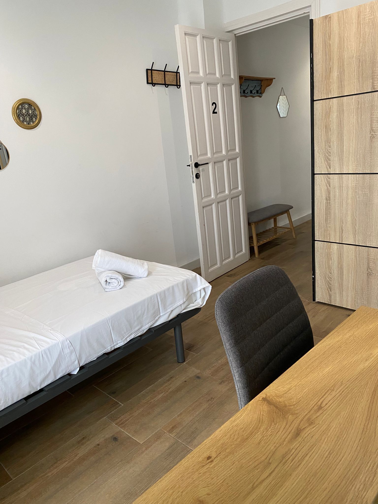 A room with a bed, a desk, a chair, a wooden cabinet, and a door with a number.