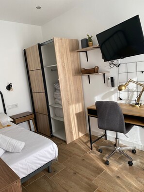 Un dormitorio con cama, escritorio y silla, armario, televisión y lámpara.