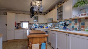 A kitchen with white cabinets, a wooden countertop, a hanging pot rack, and a tiled backsplash. - Seaside Cottage facing south overlooking Ventnor beach (Ventnor)