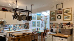 A kitchen with hanging pots, a washing machine, and a dining area with a view. - Seaside Cottage facing south overlooking Ventnor beach (Ventnor)