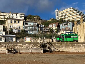 Une ville côtière avec des immeubles à plusieurs étages, un autobus vert et un escalier en pierre qui monte une colline.