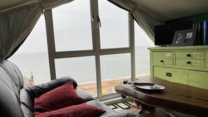 A room with a large window overlooking the sea, a green dresser, a leather sofa with red cushions, and a wooden table. - Seaside Cottage facing south overlooking Ventnor beach (Ventnor)