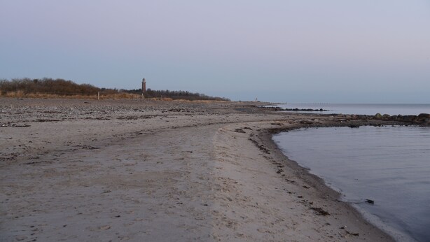 A beach with a lighthouse in the distance, sandy shore, and calm water. - Cozy vacation apartment on the Baltic Sea, with large garden (Behrensdorf (Ostsee))