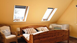 A bedroom with a wooden bed, a chair, a crib, and two skylights. - Cozy vacation apartment on the Baltic Sea, with large garden (Behrensdorf (Ostsee))