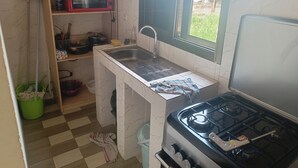 Une cuisine compacte équipée d’une cuisinière à gaz, d’un four à micro-ondes, d’un évier et d’une fenêtre donnant sur un quartier résidentiel.