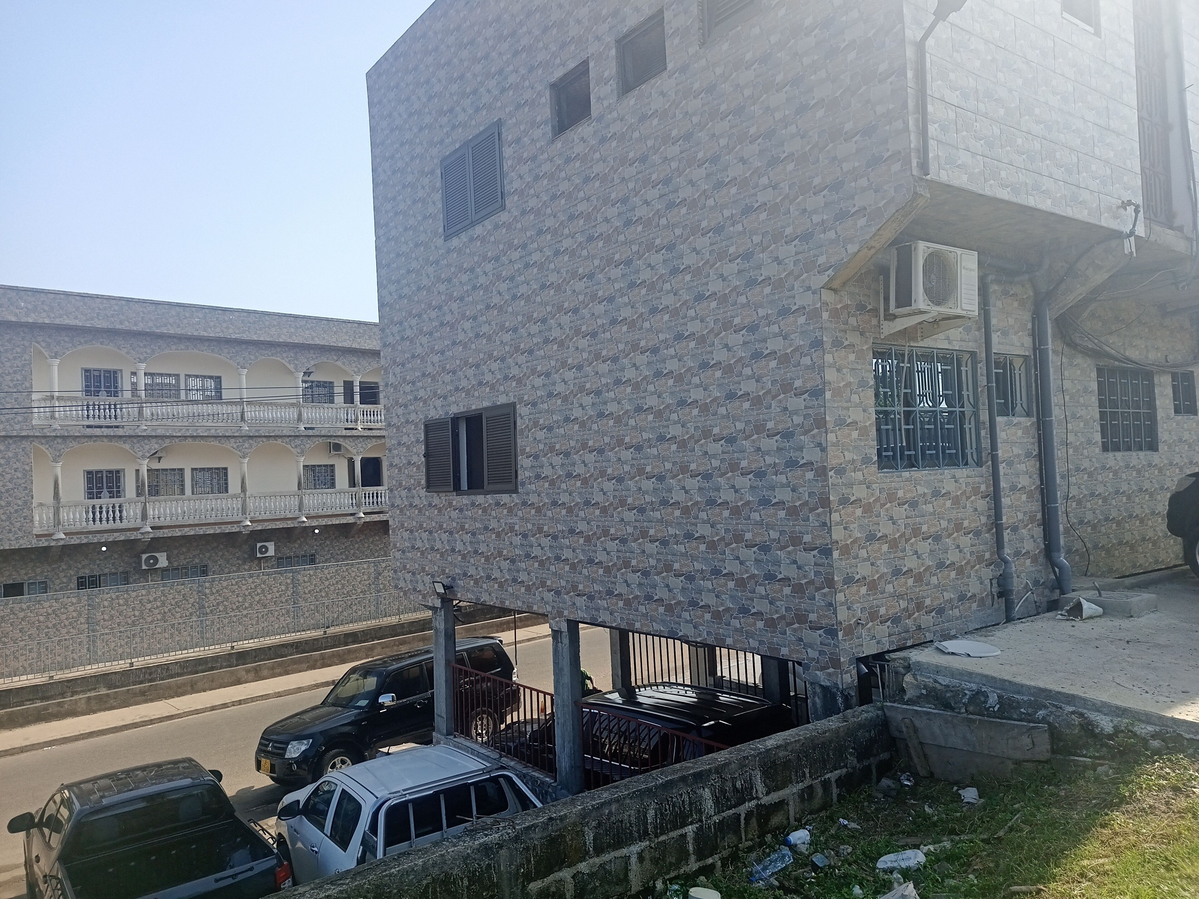 Un edificio de varios pisos con fachada de piedra, balcones y un estacionamiento con coches.