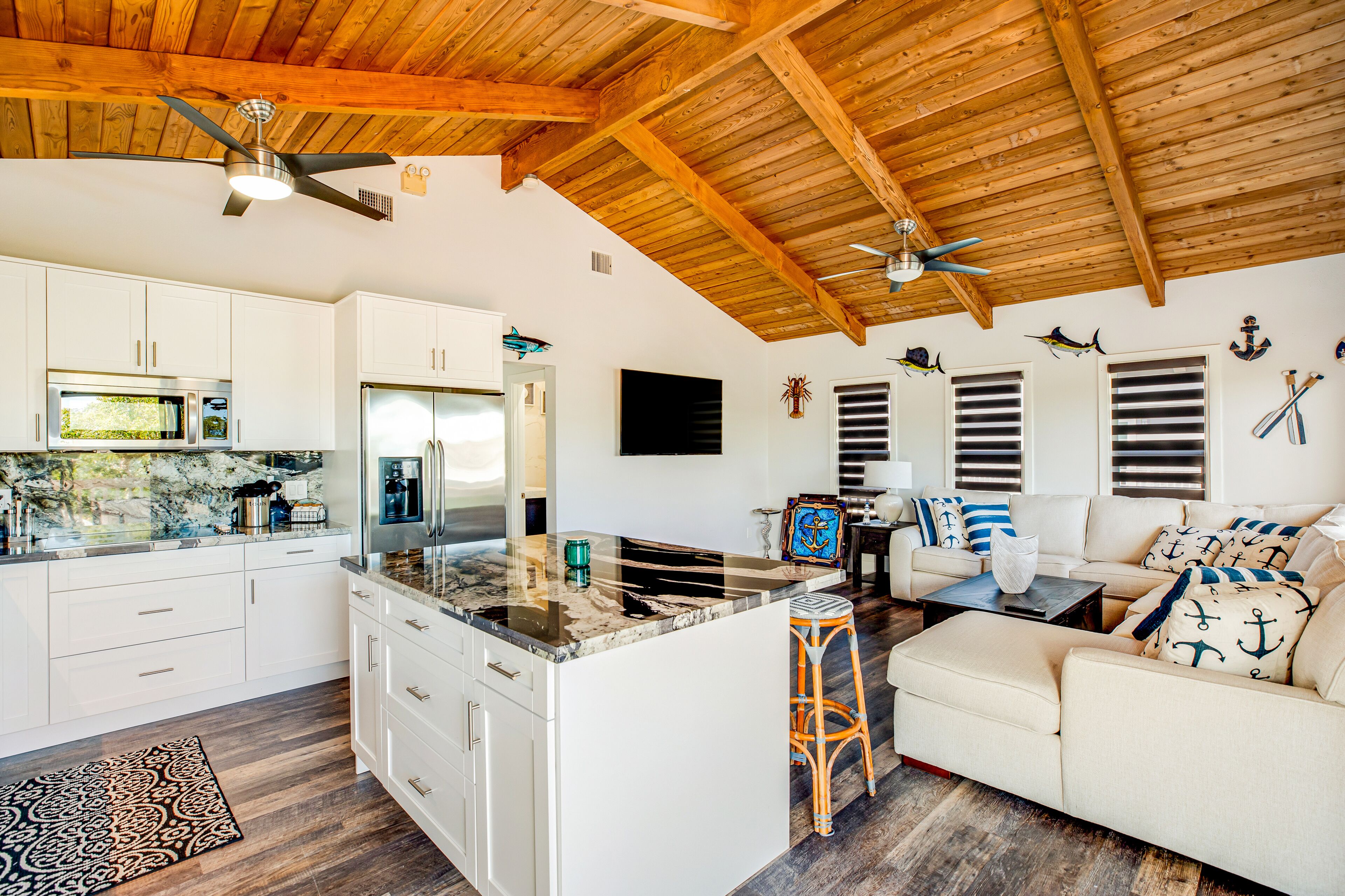 A spacious living area with a kitchen, a wooden ceiling, and nautical-themed decor.