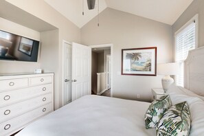 A bedroom with a bed, a dresser, a TV mounted on the wall, a painting, and a window with blinds. - Restful waterfront townhome with deck, great water views & washer/dryer (Duck Key)