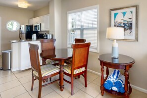 A dining area with a round table and chairs, a small side table with a lamp, and a window with blinds. - Restful waterfront townhome with deck, great water views & washer/dryer (Duck Key)