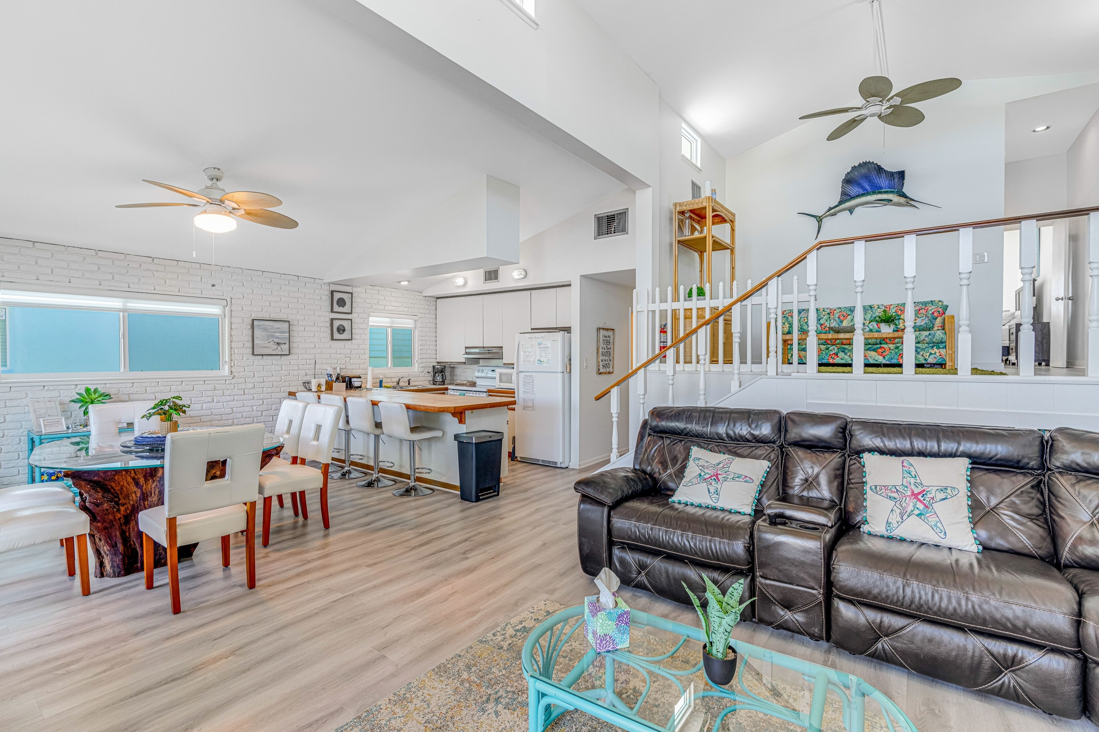 A spacious living area with a leather sofa, dining table, and chairs. A staircase with a railing leads to an upper level.