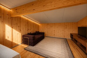 A room with wooden walls, a brown sofa, a TV stand, and a rug. - Mori House at The Retreat at Water's Edge (Tracy City)