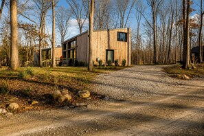 Une cabane en bois moderne, dotée d’une allée en gravier et entourée d’arbres.