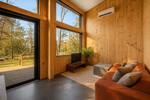 Un salon moderne avec de grandes fenêtres, un téléviseur à écran plat, un canapé et une petite table.