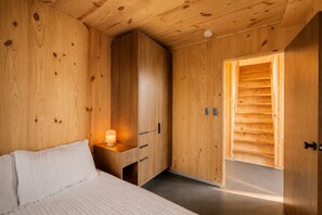 A wooden room with a bed, a bedside table with a lamp, and a wardrobe. - Mori House at The Retreat at Water's Edge (Tracy City)