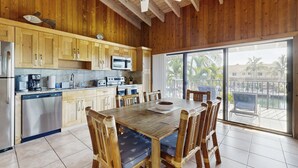 Een houten interieur met een eettafel, stoelen, een keukenhoek en een grote schuifpui naar een balkon.