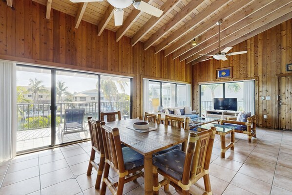 A spacious room with a wooden ceiling, large windows, a dining table with chairs, a sofa, and a television. - Charming canal-front home with 37-ft dock, kayaks, grill, patio & club access (Key Colony Beach)