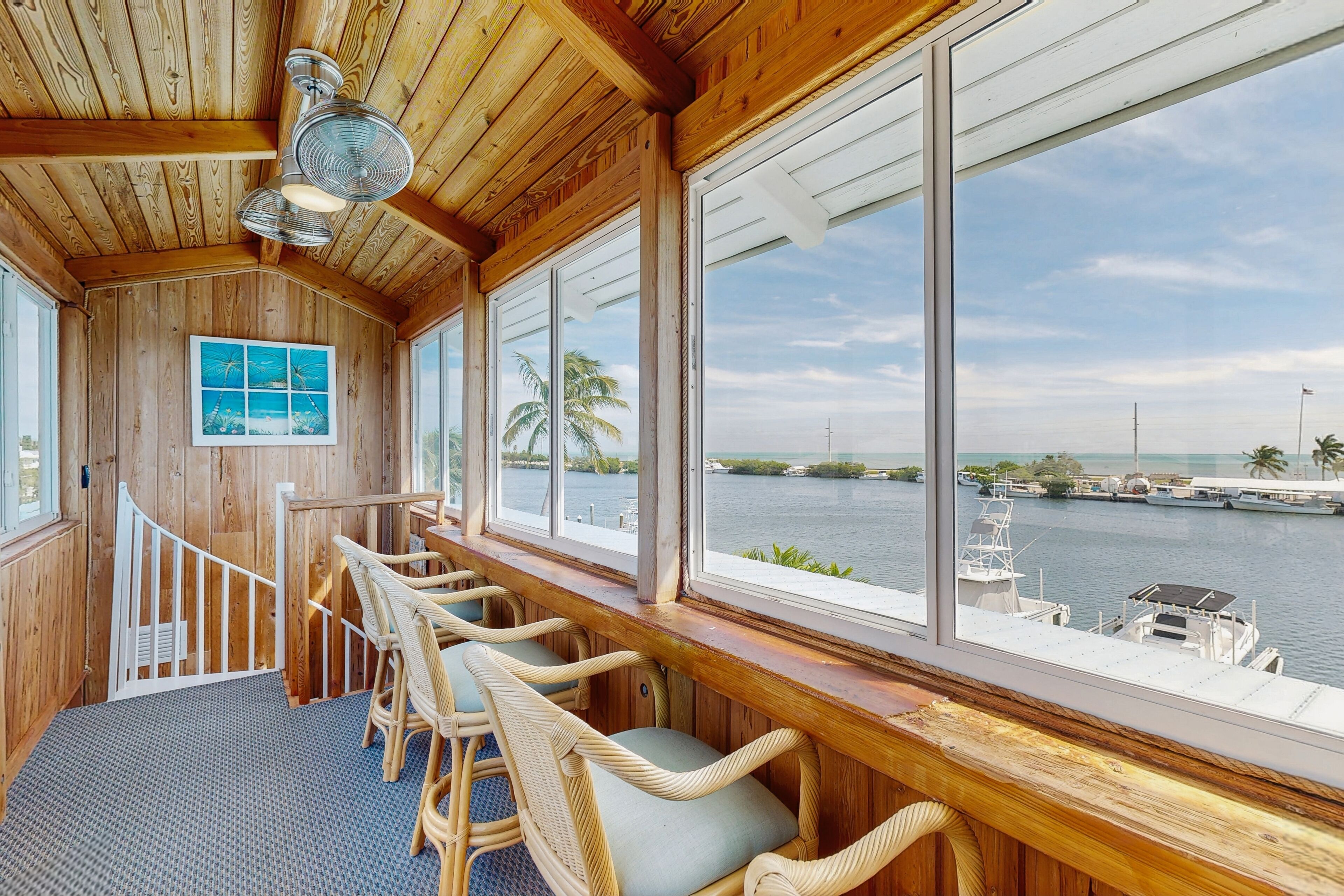 A wooden interior with a view of the water, wicker chairs, and a staircase.