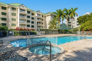 Une piscine avec un parasol, des chaises longues et un bâtiment doté de balcons en arrière-plan.