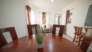 A dining area with a round wooden table, chairs, a potted plant, and a view of a living room with a sofa and curtains. - The Jungle: Private Tropical Villa : Pool & 6BR (Puerto plata)