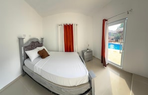 A bedroom with a bed, curtains, a nightstand, and a view of an outdoor swimming pool. - The Jungle: Private Tropical Villa : Pool & 6BR (Puerto plata)