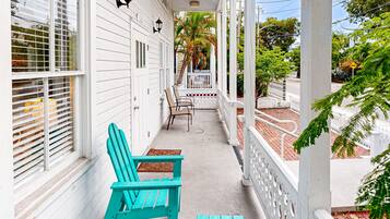 Een veranda met twee turquoise Adirondack-stoelen, een witte leuning en een palmboom op de achtergrond.