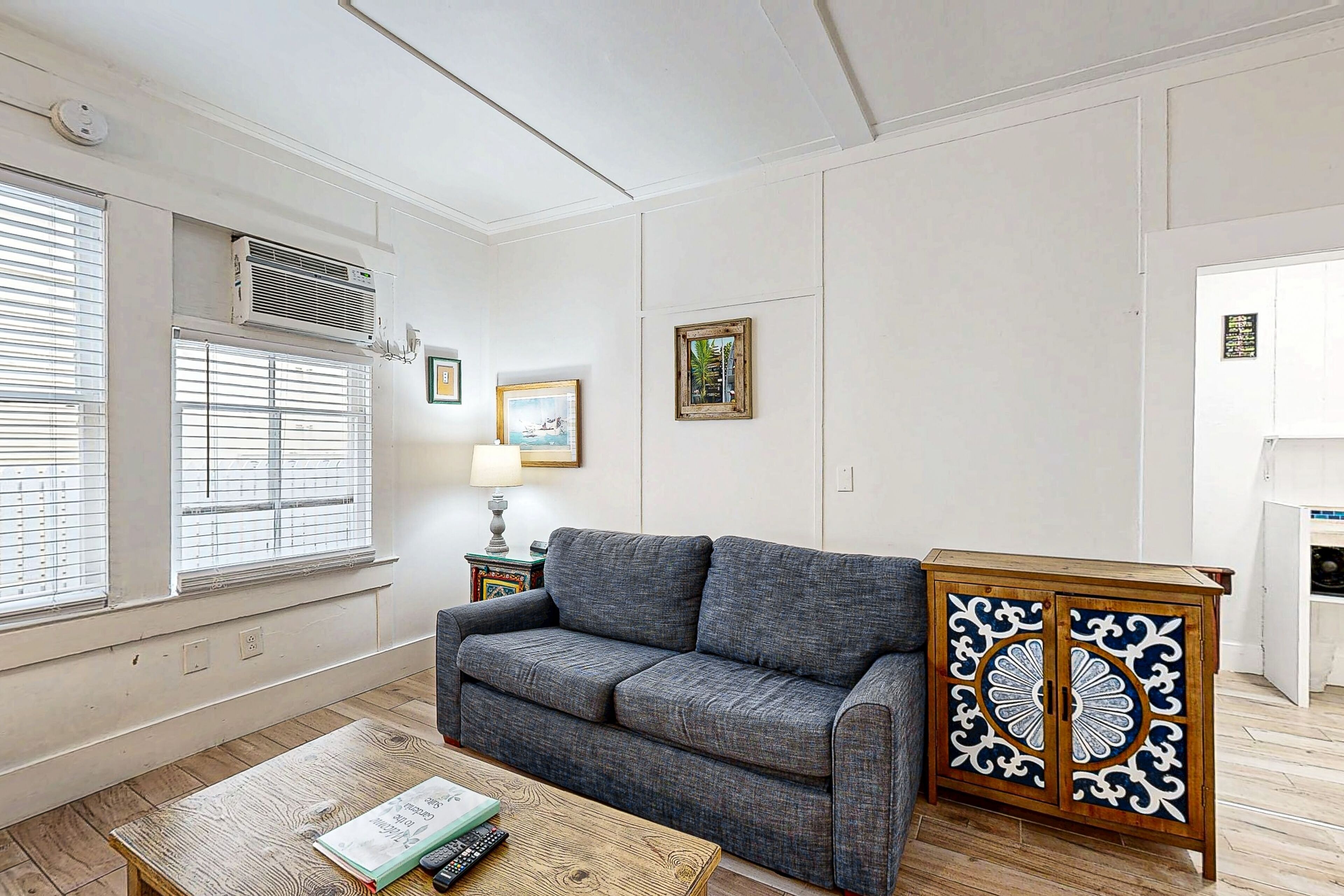 Een woonkamer met een grijze bank, een houten salontafel en een kast met decoratieve panelen.