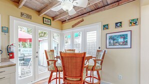 A dining area with a wooden ceiling, white walls, and a large window. There are four wicker chairs around a table, and a ceiling fan is visible. - Charming cottage with private hot tub - one block to Duvall Street (Key West)