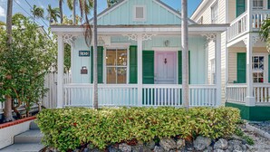 A light blue building with green shutters, a white porch, and a sign indicating it is a rental property. - Charming cottage with private hot tub - one block to Duvall Street (Key West)