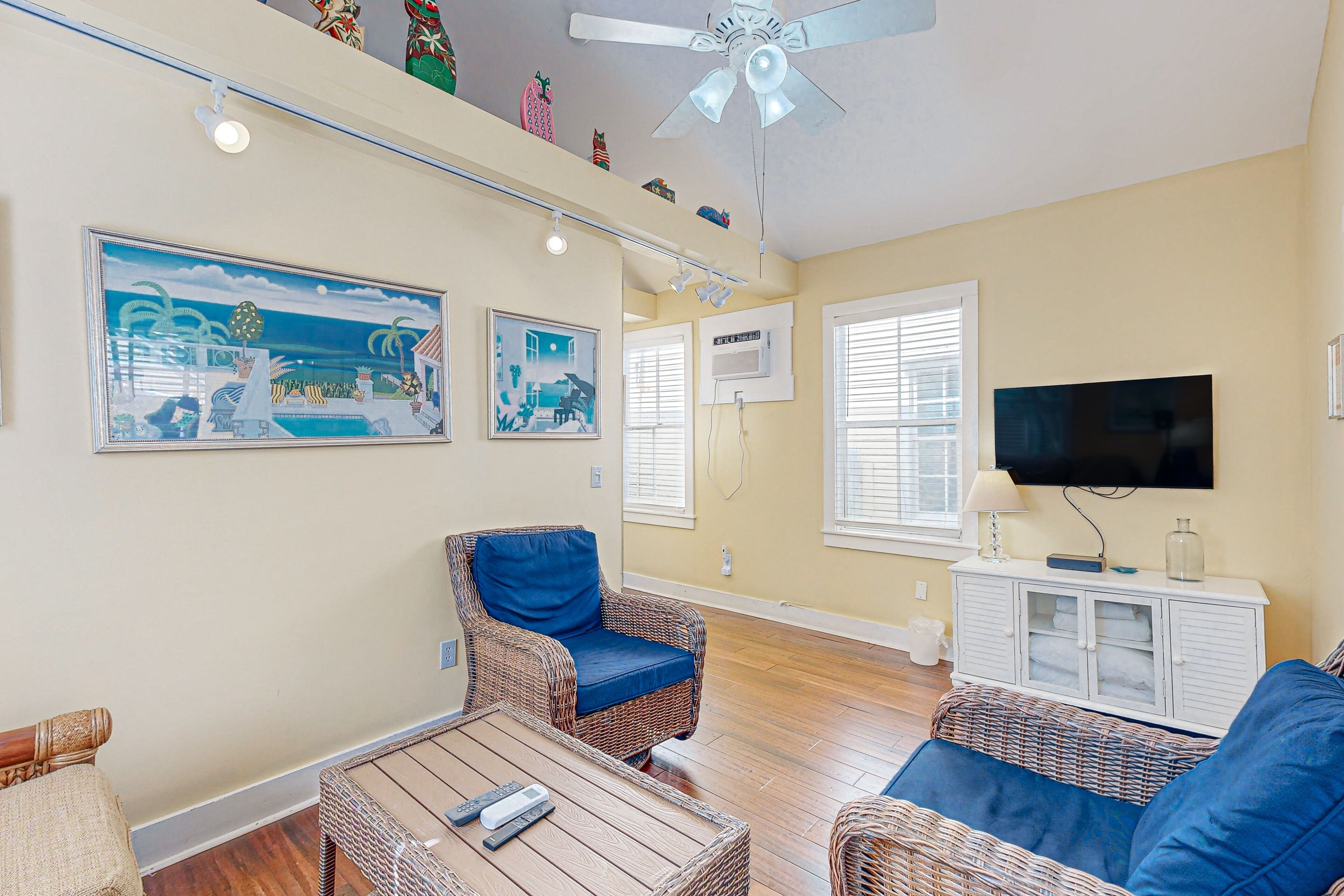 A living room with wicker furniture, a ceiling fan, and a flat-screen TV.