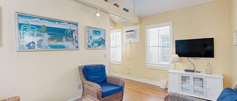 A living room with wicker furniture, a ceiling fan, and a flat-screen TV.