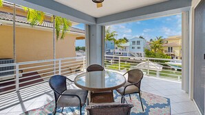 A balcony with a glass table, wicker chairs, a ceiling fan, and a view of a residential area with houses and a boat. - Canal-front, family-friendly home w/ soaking tub, dock access & water view (Key Largo)