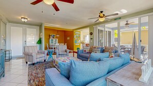 A spacious living room with a large blue sofa, striped armchairs, and a coffee table. There are ceiling fans, a dining area with chairs, and a kitchen in the background. - Canal-front, family-friendly home w/ soaking tub, dock access & water view (Key Largo)