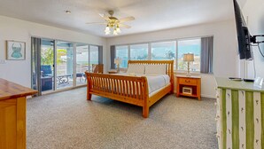 A bedroom with a wooden bed, a ceiling fan, a TV, and a view of the outdoors. - Canal-front, family-friendly home w/ soaking tub, dock access & water view (Key Largo)