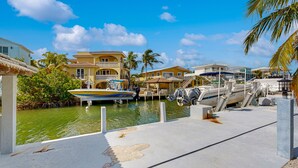 A marina with boats docked, a pool area, and buildings with balconies overlooking the water. - Canal-front, family-friendly home w/ soaking tub, dock access & water view (Key Largo)