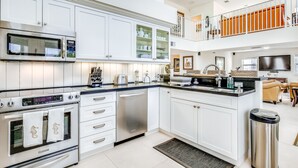 A modern kitchen with white cabinetry, stainless steel appliances, and a two-level balcony with orange railings. - Waterfront home with amazing views, boat dock, screened porch & water sport gear (Key Largo)