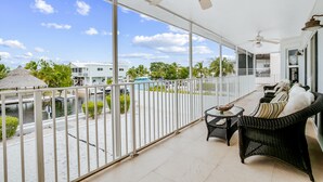 A balcony with wicker furniture, a view of the water, and a thatched-roof structure. - Waterfront home with amazing views, boat dock, screened porch & water sport gear (Key Largo)
