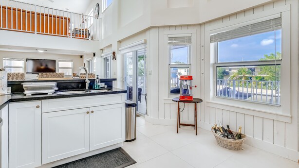 A spacious kitchen with white cabinetry, a large island, and a dining area with a view of the outdoors. - Waterfront home with amazing views, boat dock, screened porch & water sport gear (Key Largo)