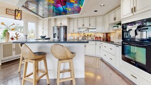 Una cocina moderna con armarios blancos, una isla central con taburetes, un refrigerador de acero inoxidable y un horno negro.