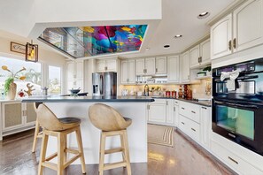 A modern kitchen with white cabinets, a central island with stools, a large refrigerator, and a black oven. - Dog-friendly home with central AC, fast WiFi, W/D, & private hot tub (Key Largo)