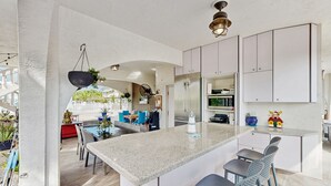 Una cocina moderna con una isla central, muebles blancos y un comedor con sillas azules.