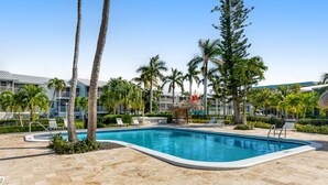 A swimming pool surrounded by palm trees and lounge chairs, with a building in the background. - Tropical condo with 2 pools, private beach area, swimming lagoon, tennis & AC (Key Largo)