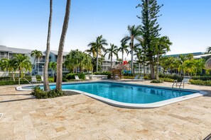 A swimming pool surrounded by palm trees and lounge chairs, with a building in the background. - Tropical condo with 2 pools, private beach area, swimming lagoon, tennis & AC (Key Largo)